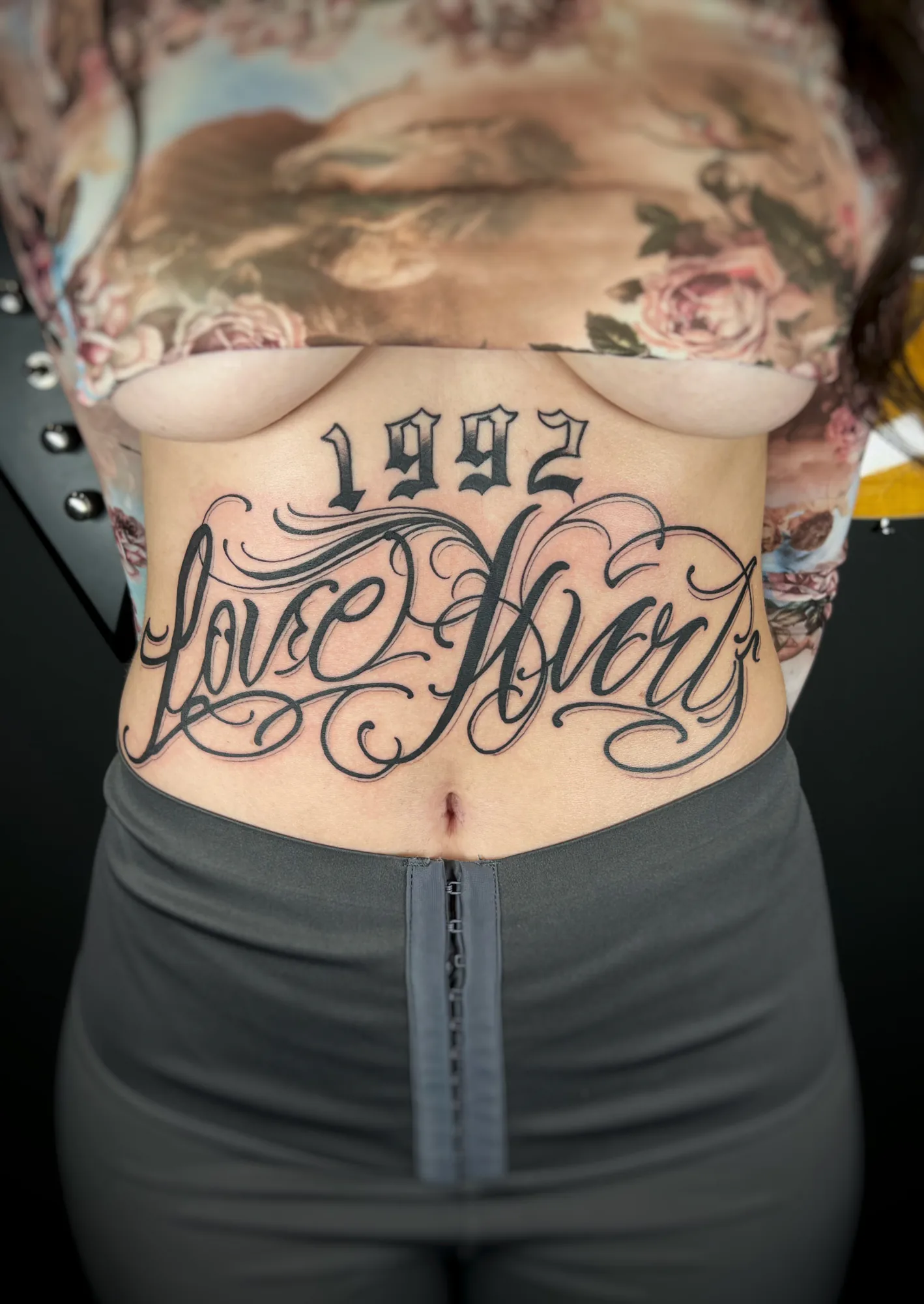 Lettering-Tattoo am Bauch: verschnörkelter Schriftzug mit Jahreszahl