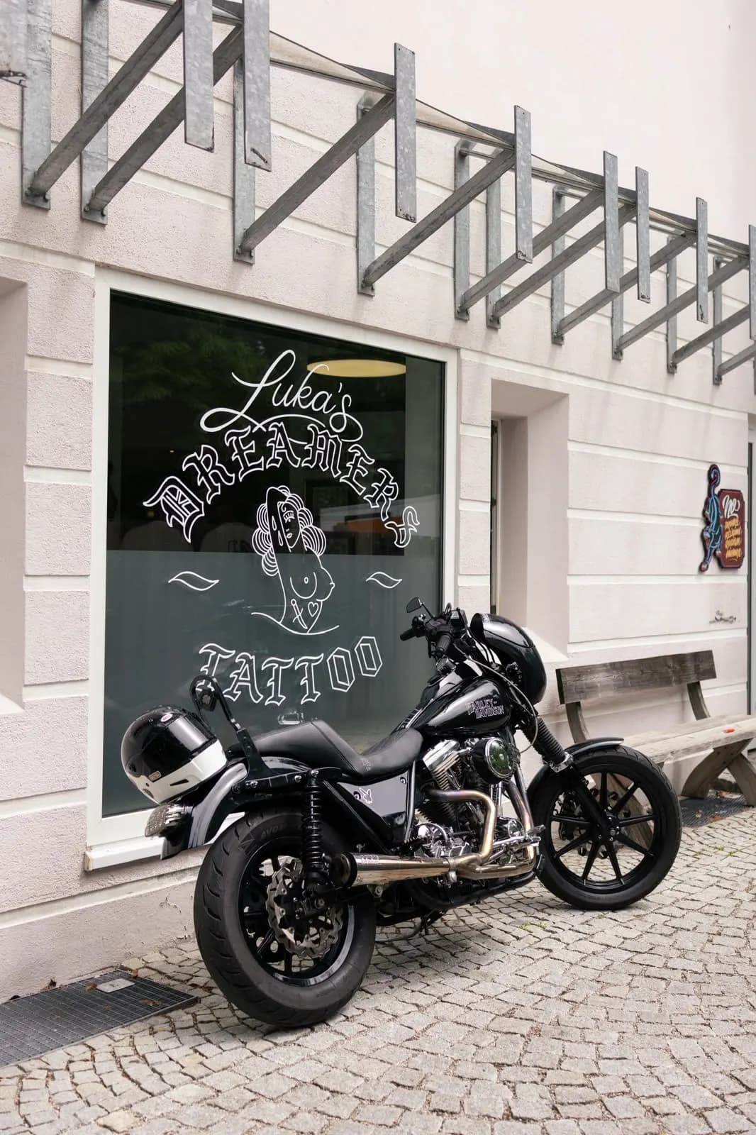 Außenansicht des Studios mit Fensterschriftzug und Motorrad vor dem Eingang