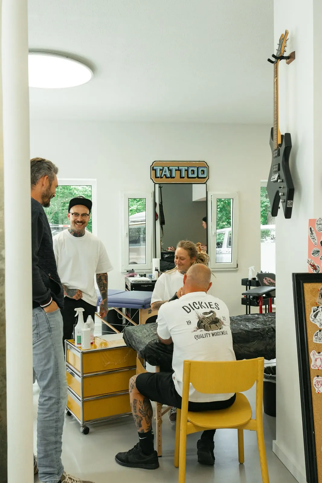 Tattoo-Arbeitsplatz mit Leuchtschild „Tattoo“ und Gitarre an der Wand